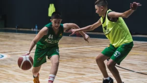 İki genç basketbolcu, basketbol akademisi'nde maç sırasında top sürüyor ve savunma yapıyor.